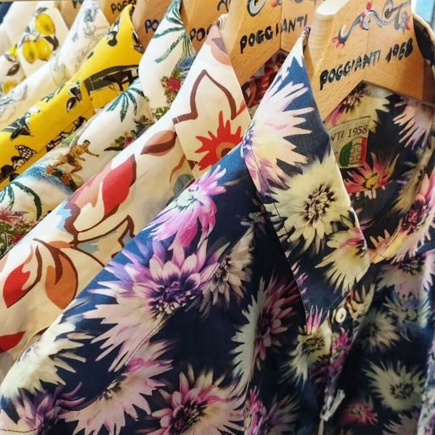 Poggianti 1958の色鮮やかな花柄シャツが木製ハンガーに並ぶ様子。イタリアらしい大胆なデザインが目を引く。