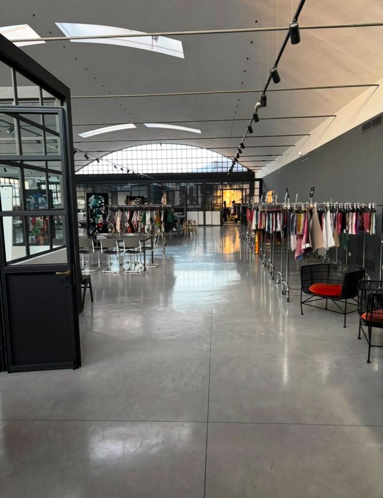 イタリア・フィレンツェのファッションショールーム。明るく洗練された空間に、最新のインポート生地やアパレルサンプルが並ぶ。バイヤー向け展示会場の雰囲気を伝える一枚。