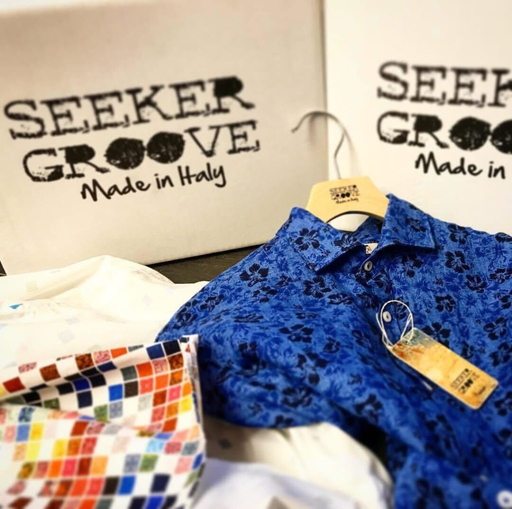 イタリア製ブランド『SEEKER GROOVE』のロゴが印刷されたボックスと、鮮やかなブルーの花柄シャツ、カラフルなプリント生地が並ぶディスプレイ