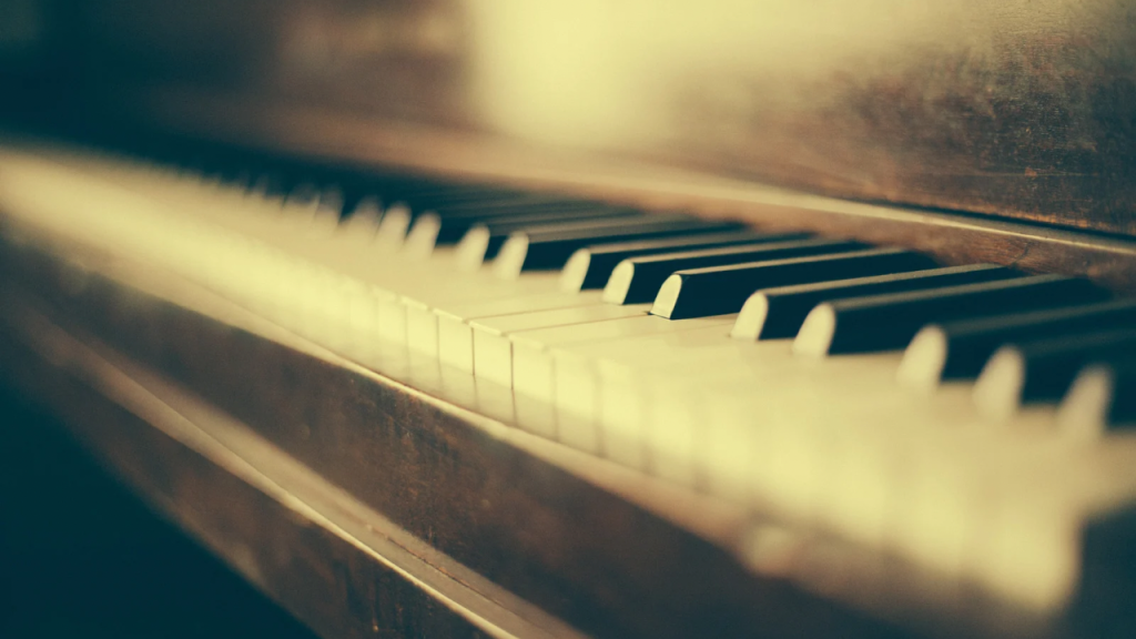 アンティークな木製ピアノの鍵盤を斜めからクローズアップで捉えた写真。柔らかな光が差し込み、ノスタルジックで温かみのある雰囲気が漂う。