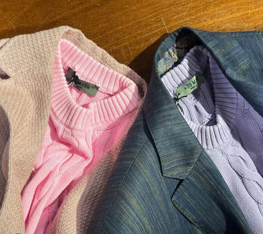 ネイビーのニットジャケットに、花柄のシャツを合わせたメンズコーディネート。胸元にはゴールドのフラワーモチーフピンがアクセントに。