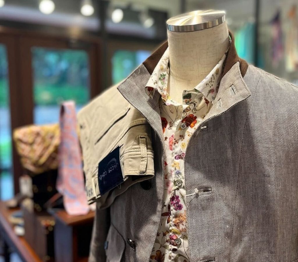 花柄プリントシャツと織り感のあるライトグレージャケットを合わせた、大人の初夏イタリアファッション。ベージュのパンツを肩掛けしたリゾート風コーデ。