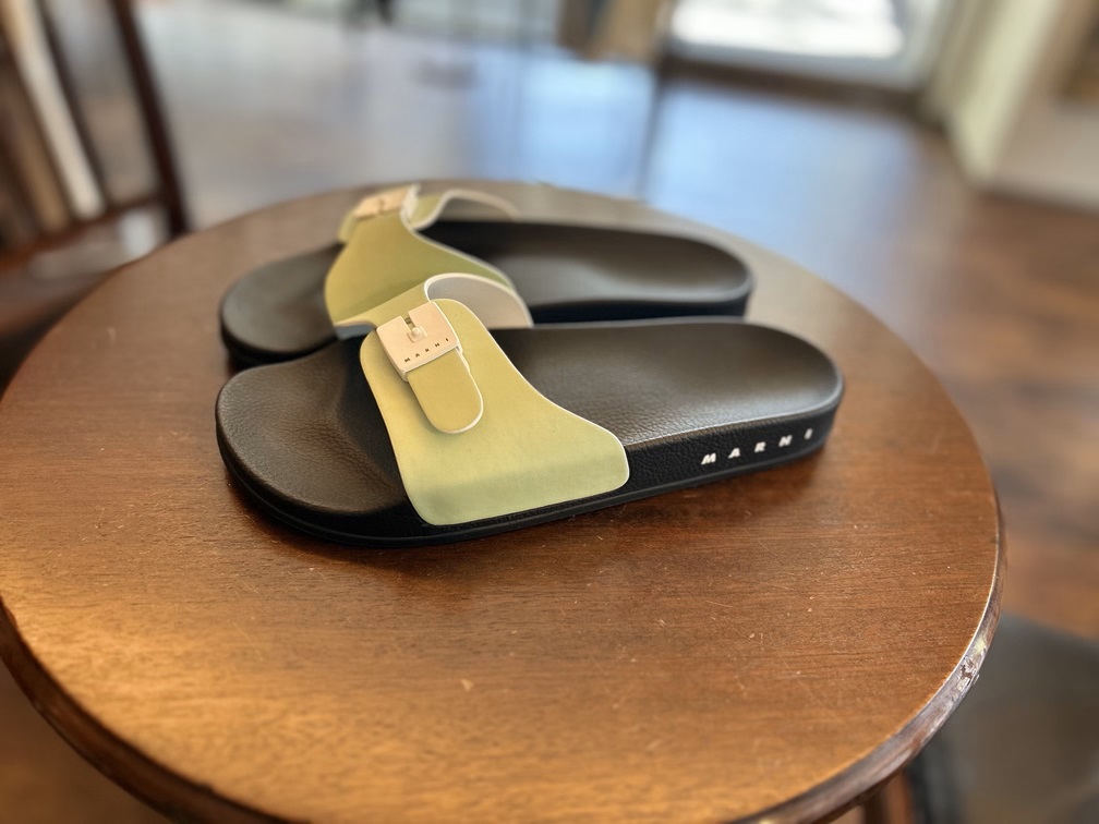 木製テーブルに置かれたイエローグリーンのMarniメンズサンダル。夏に映えるカラーで上品な抜け感を演出。