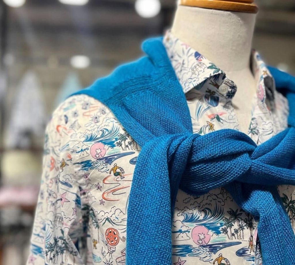 海やサーフモチーフの開襟総柄シャツに、ターコイズブルーのニットを肩掛けしたイタリアンカジュアルコーデ。25℃前後の初夏におすすめのメンズスタイル。