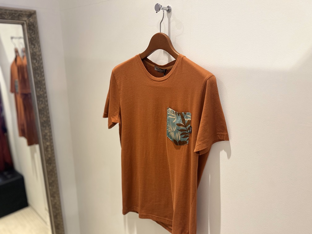 DANIELE ALESSANDRINIのオレンジTシャツが壁に掛けられたディスプレイ画像