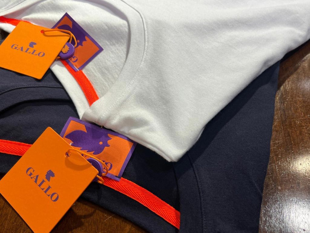 Galloブランドの白とネイビーのTシャツがテーブルの上に並べられているクローズアップショット。オレンジと紫のブランドタグ付き。