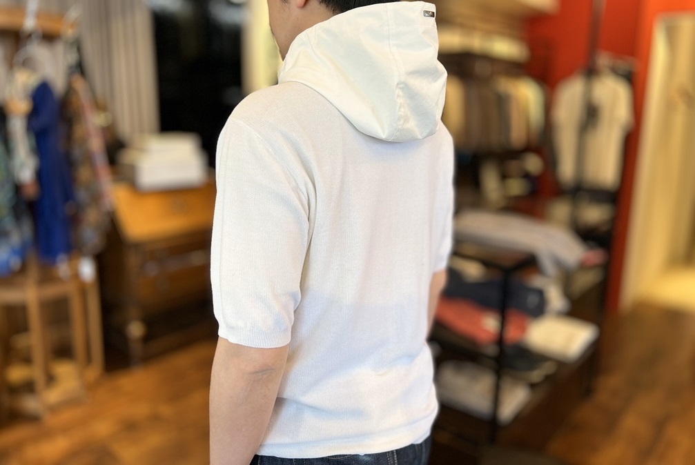 HERNOの半袖ニットパーカーを着用した後ろ姿。フードと袖のバランス感、ロゴ入りメタルパーツが見える角度