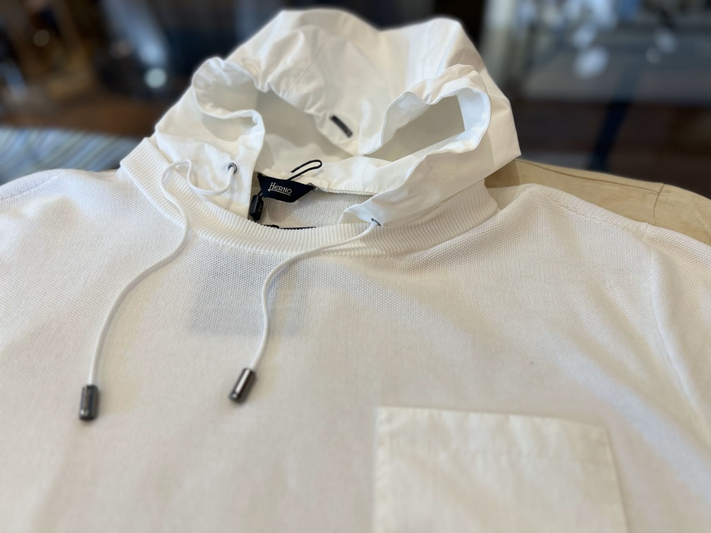 HERNOの半袖ニットパーカーを平置きで撮影したフード部分のディテール。ロゴ入り金属パーツとドローコードが確認できる構図