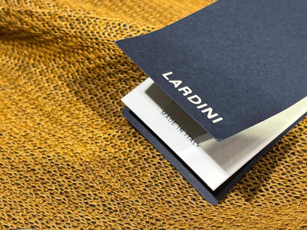 LARDINIのタグが添えられた、イタリア製のラグジュアリーなニット生地のクローズアップ画像。黄味がかったゴールドの編地が高級感を演出。