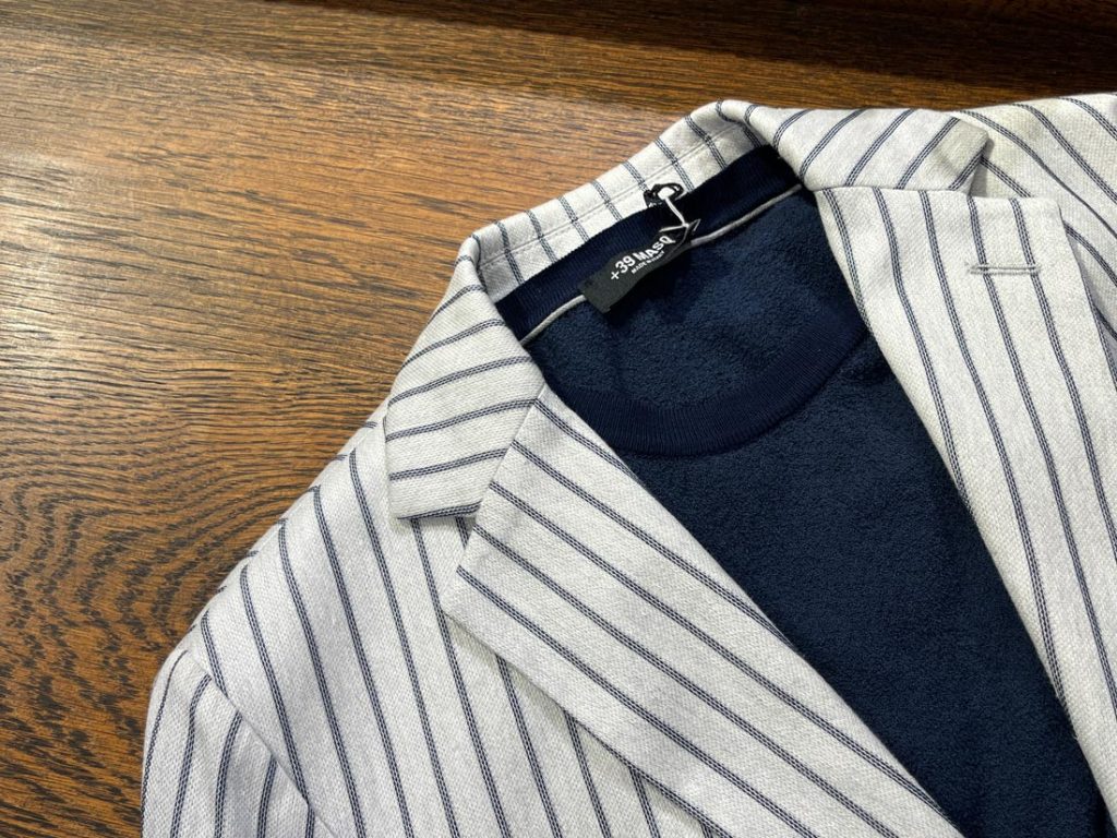 +39 masqのライトグレーストライプジャケットに、ネイビーのカットソーを合わせた爽やかなレイヤードスタイル。春夏の軽快な着こなしに最適。