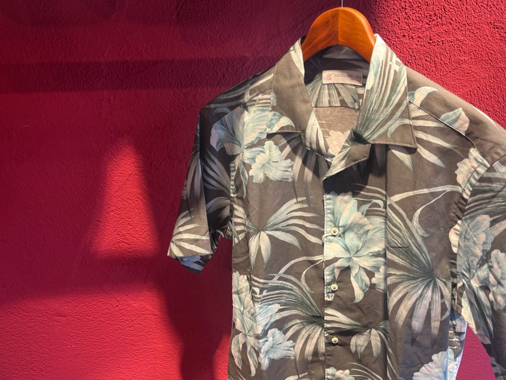 POGGIANTI 1958のフラワープリントオープンカラーシャツが赤い壁を背景にハンガーに掛けられているディスプレイ画像