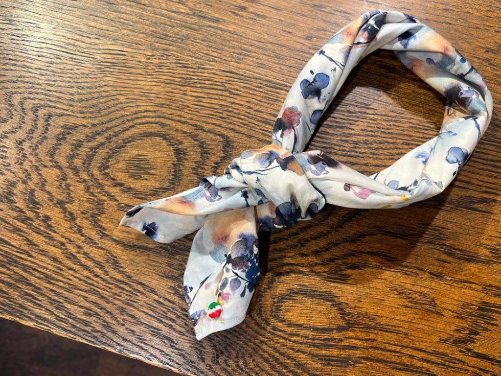 水彩画のような花柄ネッカチーフを結んだカット。淡い色調が首元にやわらかな陰影を作り、夏のTシャツも上品に見せる。