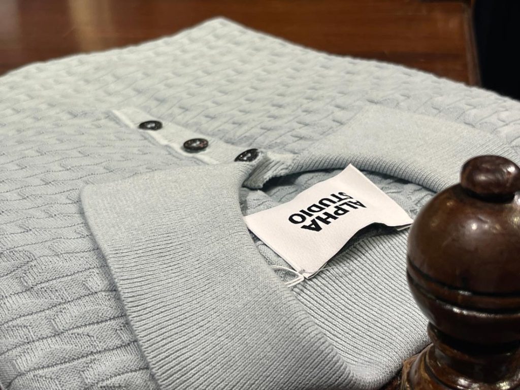 ALPHA STUDIOのニットポロシャツ。繊細な編み込み模様と上品なボタンデザインが特徴的な一着。