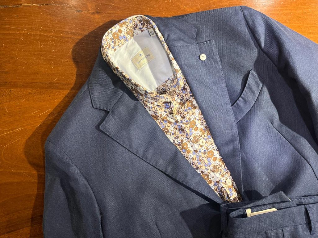 ネイビージャケットに合わせたBASTONCINOのフローラルプリントシャツ。落ち着いたブルーとブラウンの花柄が印象的で、大人のエレガンスと遊び心を併せ持つイタリアンコーディネート。