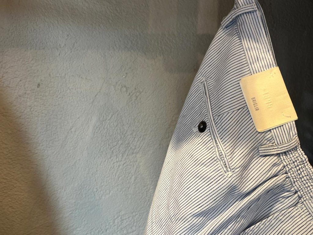 BRIGLIAのストライプ柄パンツ。バックポケットにブランドタグが付き、ドローコードとシャーリング仕様が見える後ろ姿のディテール。