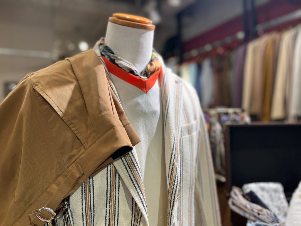 ストライプ柄ジャケットにブラウンのパンツを合わせた春夏スタイル。首元にはスカーフを巻き、上品で軽やかなイタリアンコーデを演出。