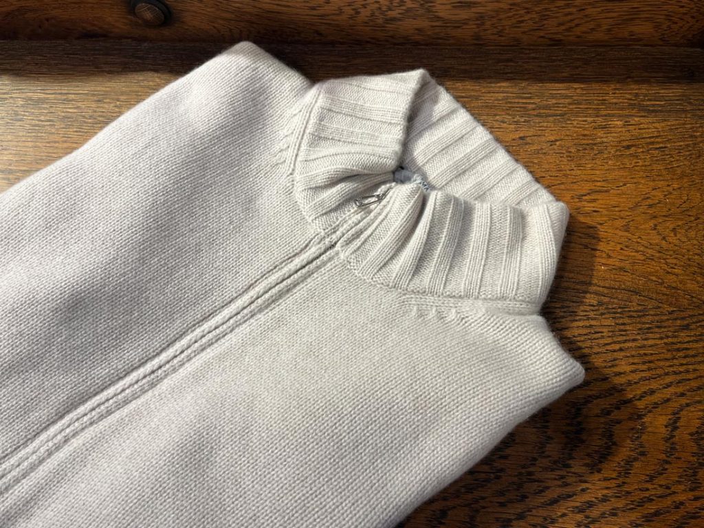 LAMANO ARTISANSのジップアップニット。ライトグレーの無地ボディに太めのリブ襟が特徴のシンプルな上質アイテム。
