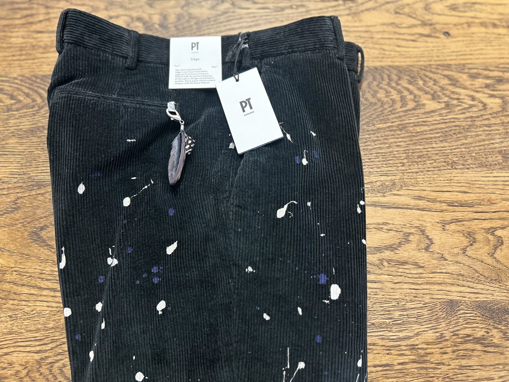 平置きされたPT TORINO ブラックコーデュロイパンツ 羽のチャーム付き