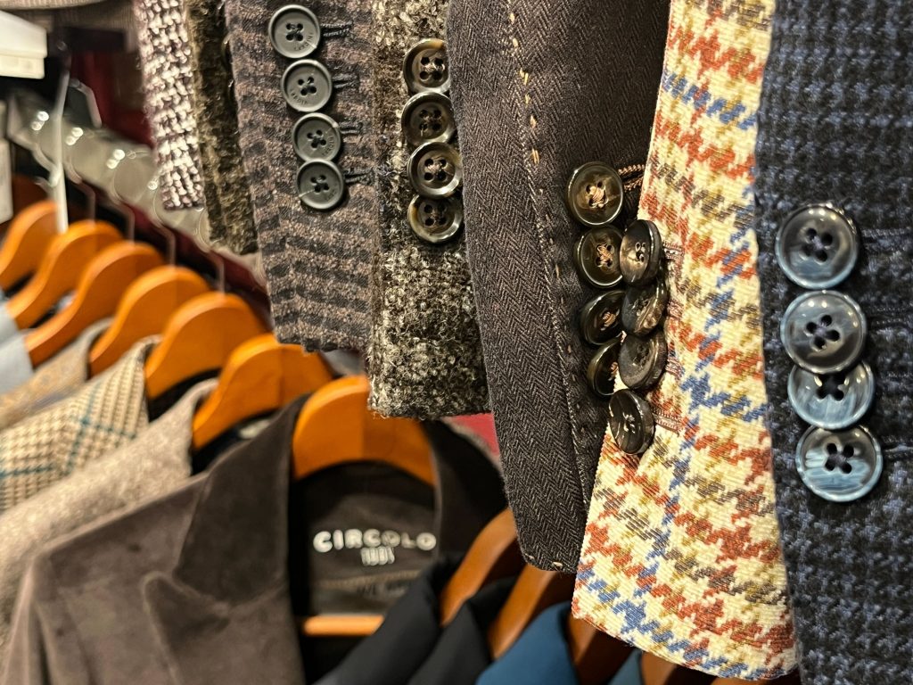 秋冬ジャケットの袖口のボタンディテール。多彩なツイードやチェック柄が並び、各ジャケットの表情と職人技が際立つ。