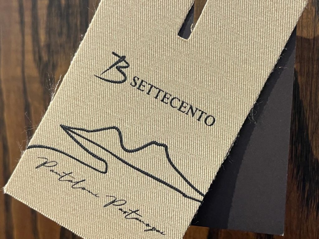 B SETTECENTOのブランドロゴが刻印されたタグ、クラシカルな印象のパンツタグデザイン