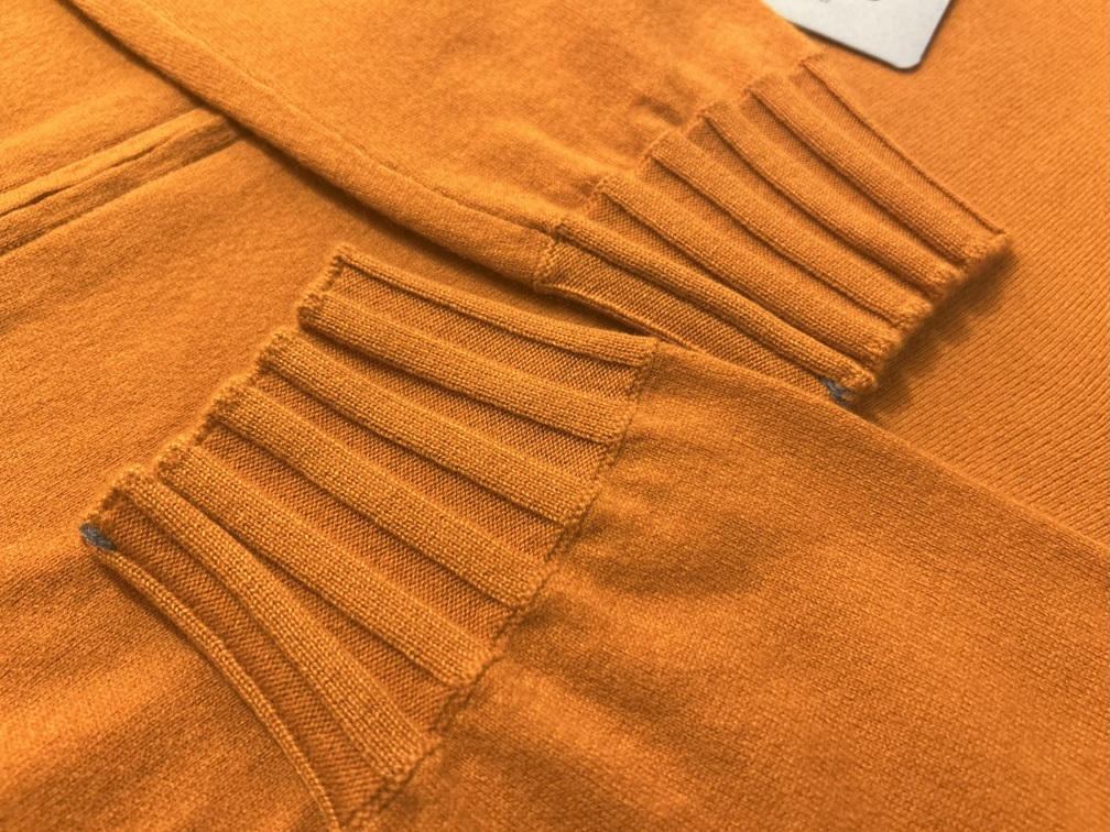 袖口と裾の幅広リブが立体感を生むオレンジニットの質感