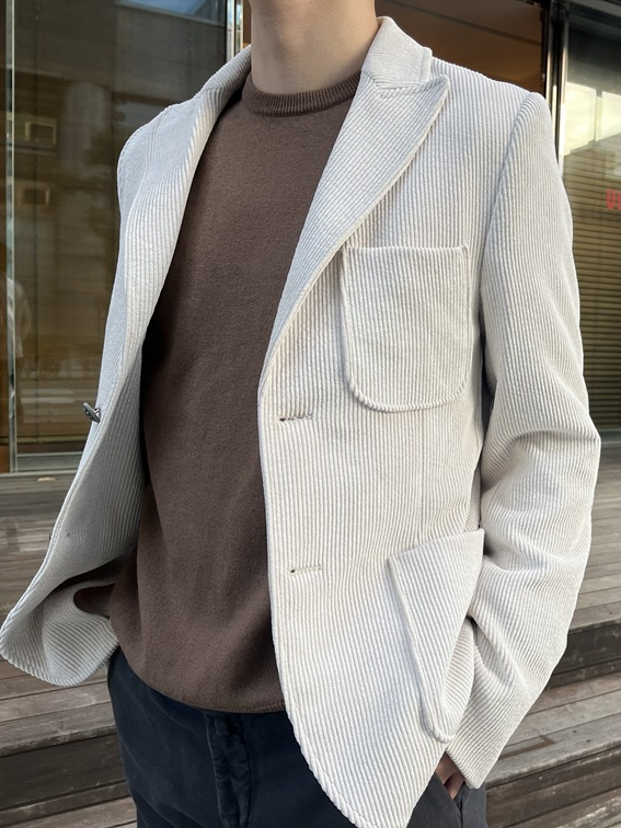 アイボリーのコーデュロイジャケットにブラウンのクルーネックニットを合わせた上品なスタイル(アップ)。異素材の組み合わせが温かみと立体感を演出。