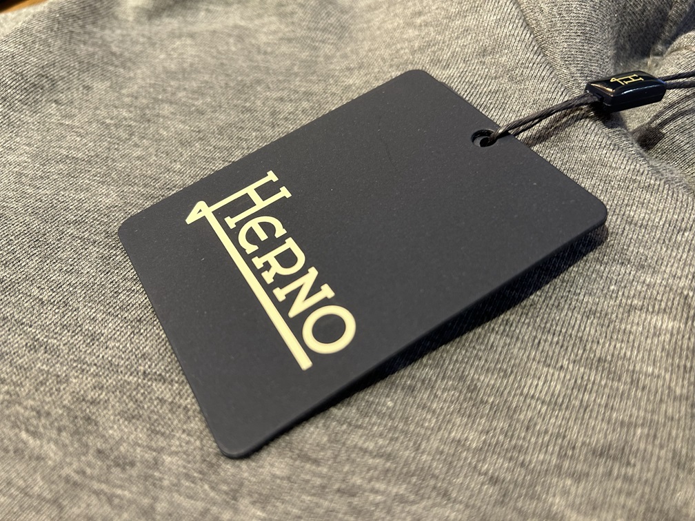 HERNOのブランドタグを写したクローズアップカット。グレーの生地に映えるロゴが上品な雰囲気を引き立てる。