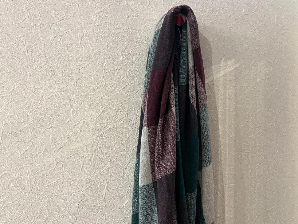 グリーン×レッド系のDANIELE FIESOLIマフラーが壁に掛けられている様子