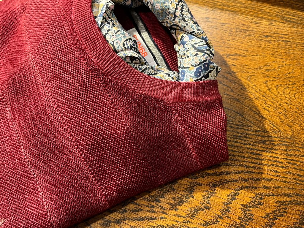 SAN68のボルドーニットにネッカチーフをレイヤードしたスタイリング。編地の切り替えが奥行きを生む。