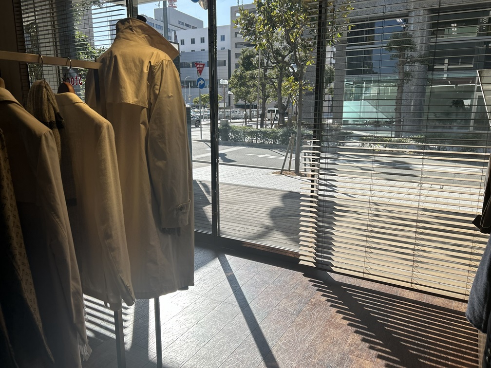 店内に並ぶ春コートと差し込む光。冬から春への視覚的な移ろいを表現。
